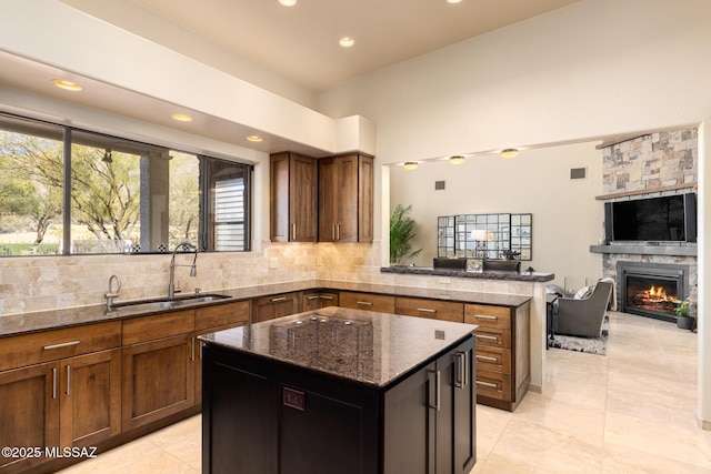 kitchen featuring sink, a stone fireplace, dark stone counters, and a kitchen island