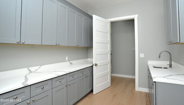 kitchen with gray cabinetry, light stone counters, and sink