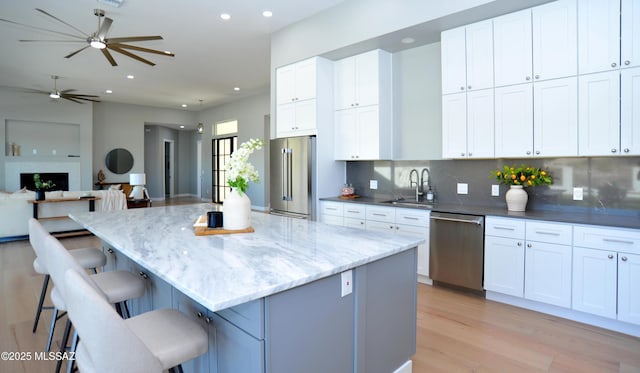 kitchen featuring a kitchen breakfast bar, stainless steel appliances, a kitchen island, sink, and white cabinetry