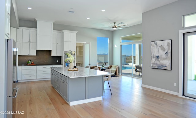 kitchen with light stone counters, a kitchen island, stainless steel refrigerator, white cabinetry, and a breakfast bar area