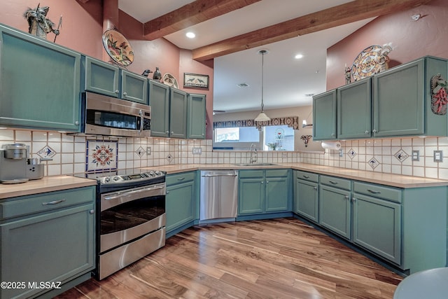 kitchen with a sink, light countertops, appliances with stainless steel finishes, beam ceiling, and decorative light fixtures