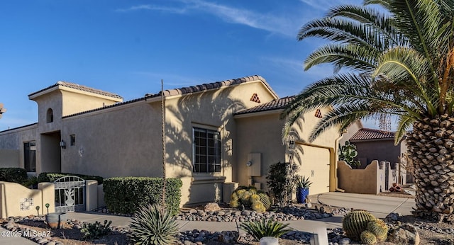 mediterranean / spanish home featuring a garage, driveway, a tiled roof, a gate, and stucco siding