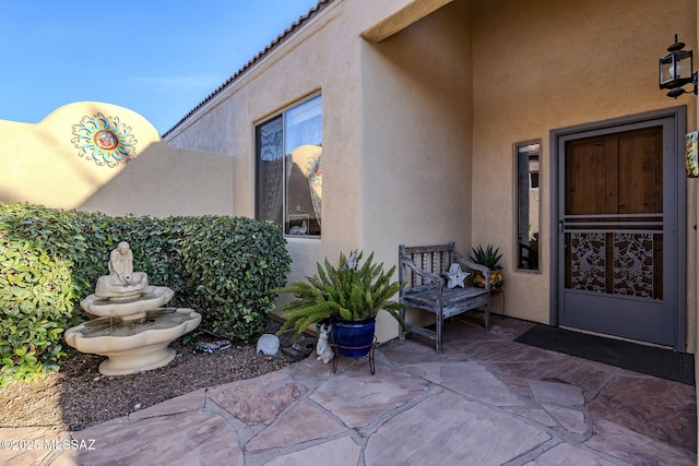 doorway to property with a patio area, a tile roof, and stucco siding