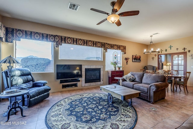 tiled living room featuring visible vents, a tiled fireplace, and ceiling fan with notable chandelier