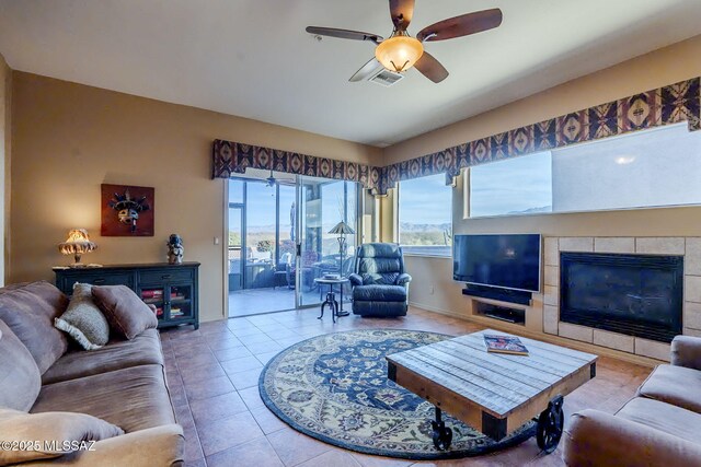 living room featuring ceiling fan, a fireplace, visible vents, and tile patterned floors