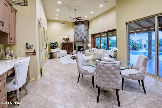 dining space with light tile patterned floors, a towering ceiling, a fireplace, and ceiling fan