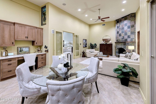 dining space featuring a fireplace, a high ceiling, ceiling fan, and light tile patterned flooring