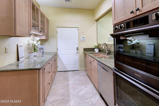 kitchen featuring sink, light tile patterned floors, dishwasher, double oven, and dark stone counters