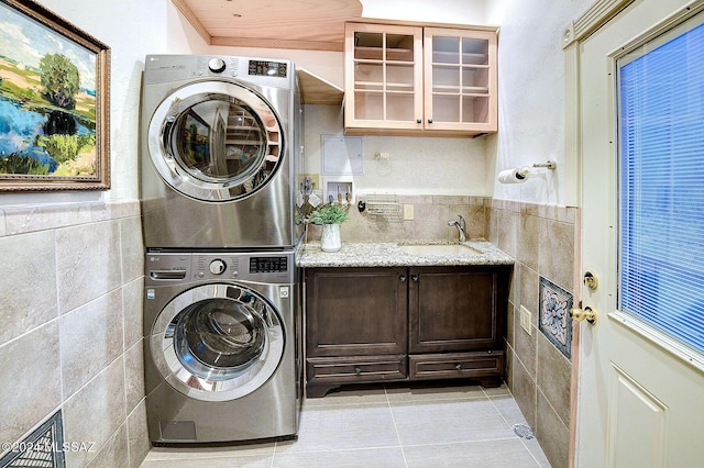 clothes washing area with light tile patterned flooring, tile walls, stacked washer / dryer, and sink