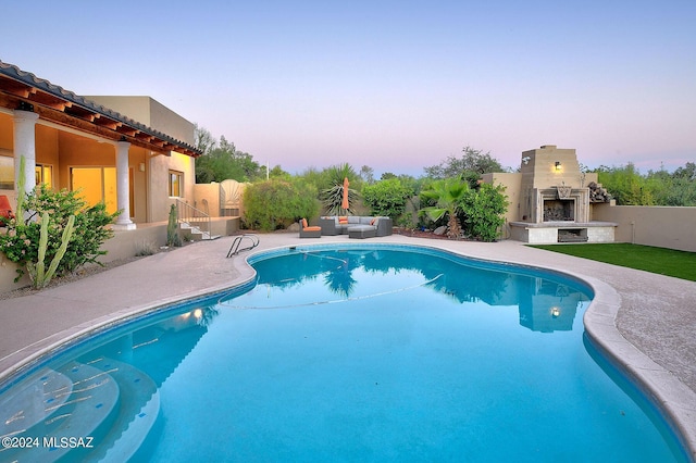 pool at dusk featuring an outdoor living space with a fireplace and a patio area