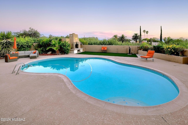 pool at dusk featuring a patio area and an outdoor fireplace