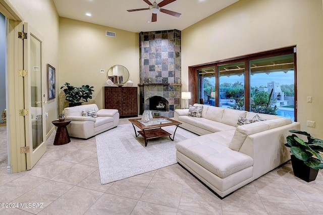 living room featuring a tiled fireplace, light tile patterned floors, high vaulted ceiling, and ceiling fan