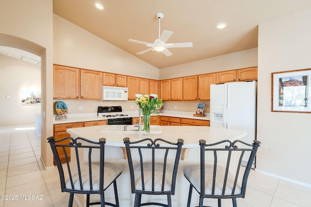 kitchen with light tile patterned floors, white appliances, a kitchen island with sink, and ceiling fan