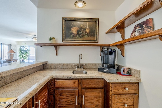 kitchen featuring brown cabinets, light stone counters, open shelves, and a sink