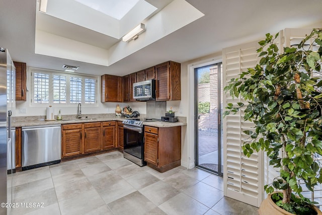 kitchen with a wealth of natural light, a raised ceiling, stainless steel appliances, light countertops, and a sink