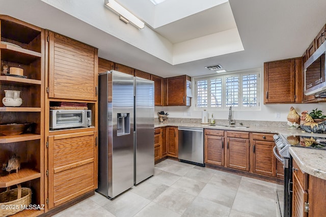 kitchen featuring a sink, light countertops, appliances with stainless steel finishes, brown cabinets, and open shelves