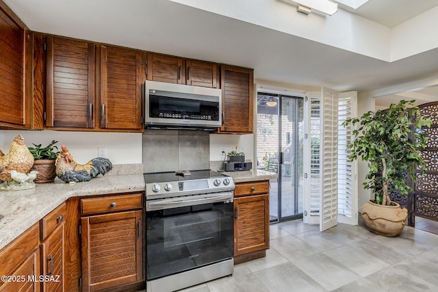 kitchen featuring stainless steel appliances, brown cabinetry, and light stone countertops