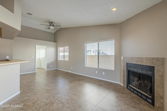 unfurnished living room with ceiling fan, vaulted ceiling, a tile fireplace, a textured ceiling, and light tile patterned floors