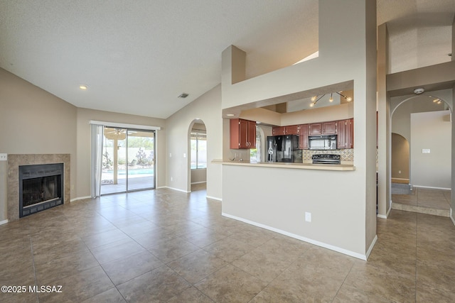 kitchen with black appliances, kitchen peninsula, decorative backsplash, a tiled fireplace, and high vaulted ceiling