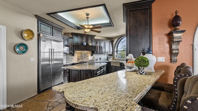 kitchen with a center island, a kitchen breakfast bar, decorative backsplash, light stone countertops, and appliances with stainless steel finishes