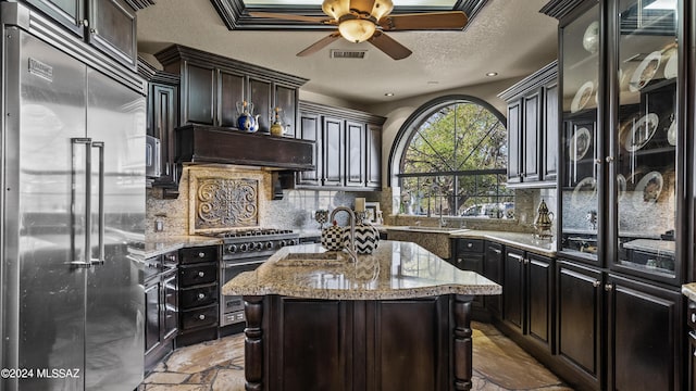 kitchen featuring high end appliances, backsplash, light stone countertops, a kitchen island, and custom range hood