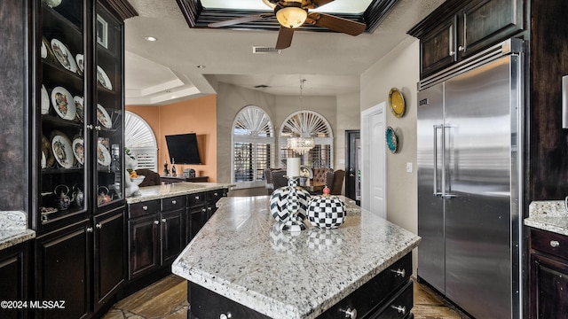 kitchen featuring built in fridge, ceiling fan, a kitchen island, and light stone counters