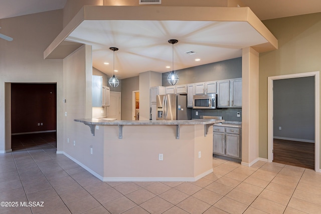 kitchen with kitchen peninsula, hanging light fixtures, light tile patterned floors, a breakfast bar area, and appliances with stainless steel finishes