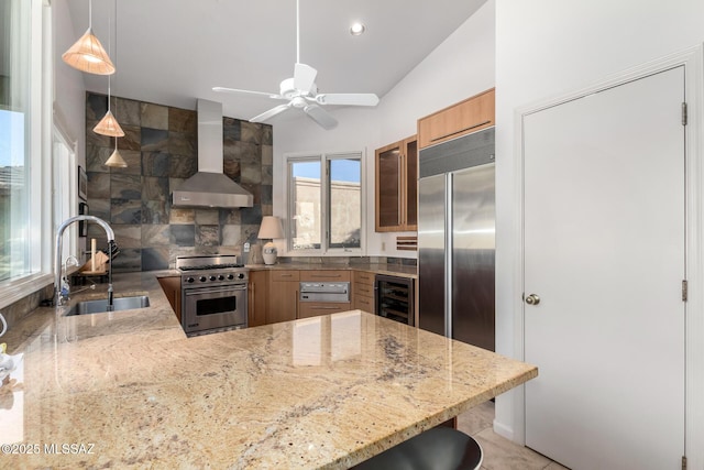 kitchen featuring wall chimney range hood, high end appliances, sink, kitchen peninsula, and a breakfast bar