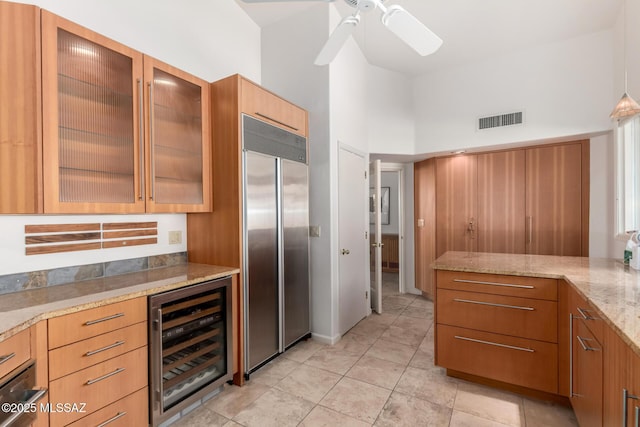 kitchen featuring wine cooler, ceiling fan, a high ceiling, stainless steel built in fridge, and light stone counters