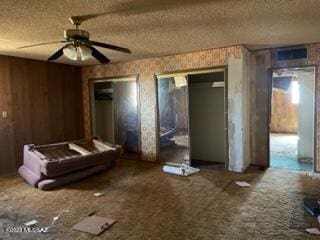 interior space with a textured ceiling, ceiling fan, and wood walls