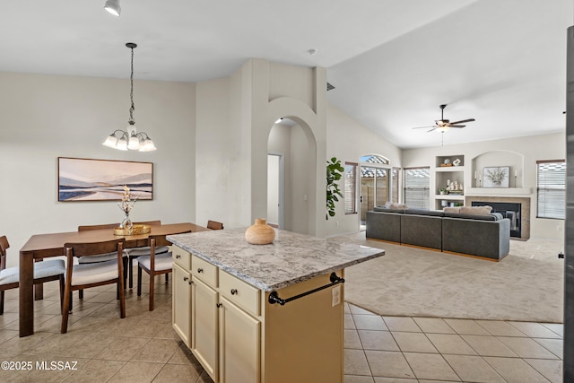 kitchen with a fireplace, a center island, light stone counters, cream cabinets, and light carpet