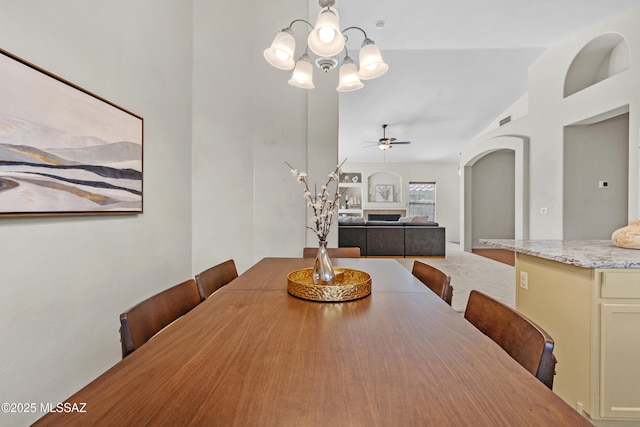 dining room featuring light colored carpet, lofted ceiling, and ceiling fan with notable chandelier