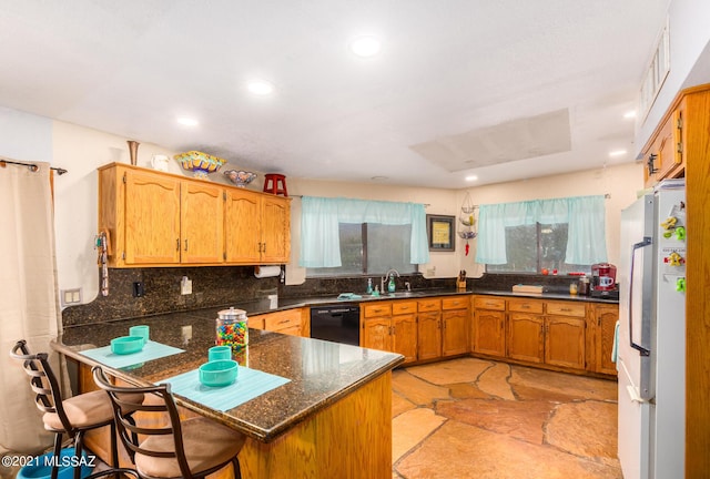 kitchen featuring kitchen peninsula, a kitchen bar, backsplash, white refrigerator, and dishwasher