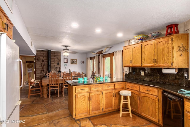 kitchen with kitchen peninsula, backsplash, white refrigerator, black dishwasher, and a wood stove