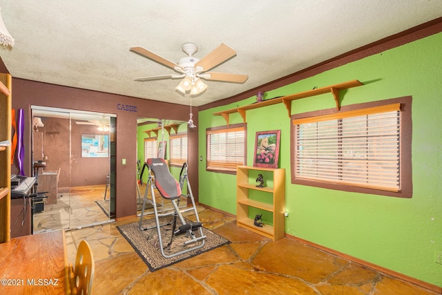 exercise area with ceiling fan and a textured ceiling