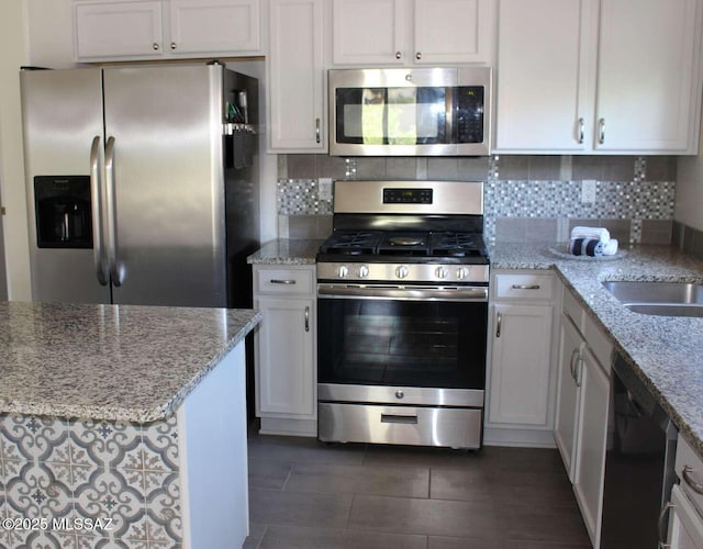 kitchen featuring white cabinets, stainless steel appliances, a sink, light stone counters, and backsplash