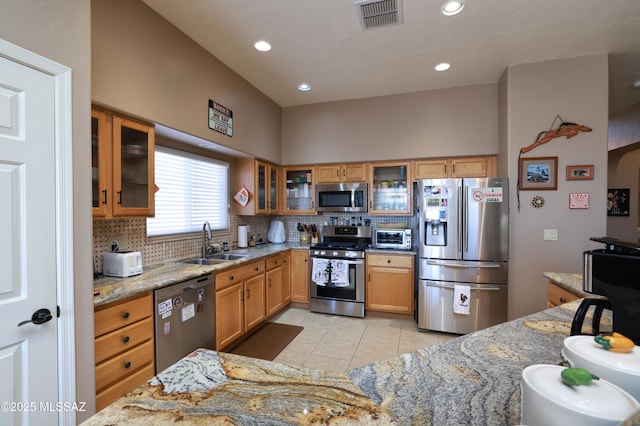 kitchen with sink, light stone countertops, light tile patterned floors, tasteful backsplash, and stainless steel appliances