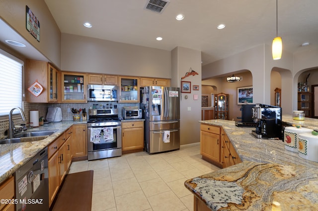 kitchen featuring light stone countertops, sink, stainless steel appliances, tasteful backsplash, and decorative light fixtures