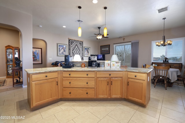 kitchen featuring light stone counters, ceiling fan with notable chandelier, light tile patterned floors, decorative light fixtures, and a center island