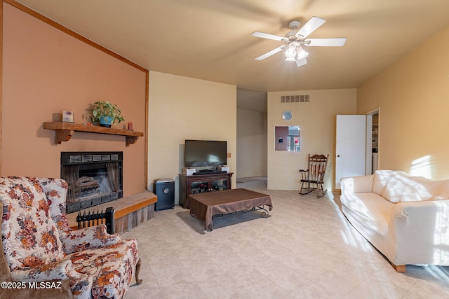 living area with a fireplace with raised hearth, ceiling fan, and visible vents