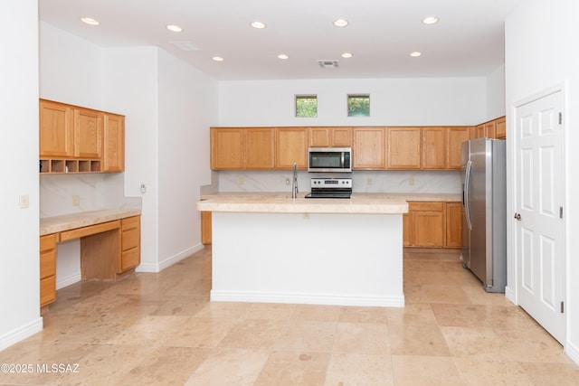 kitchen with stainless steel appliances, a center island with sink, built in desk, and tasteful backsplash