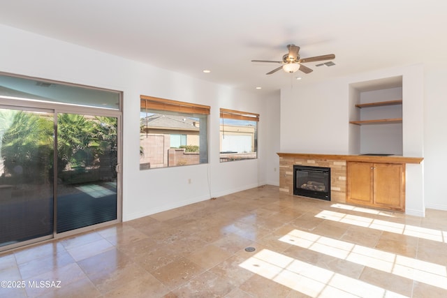 unfurnished living room with a tiled fireplace, ceiling fan, and a healthy amount of sunlight