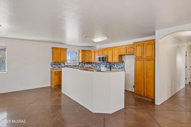 kitchen featuring appliances with stainless steel finishes, backsplash, and a kitchen island with sink