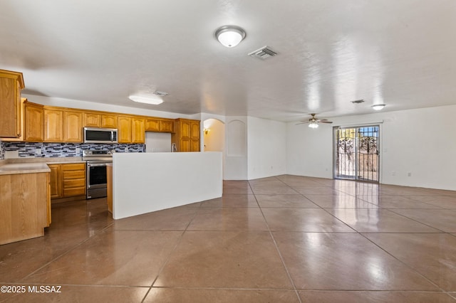 kitchen with backsplash, tile patterned flooring, ceiling fan, a kitchen island, and stainless steel appliances