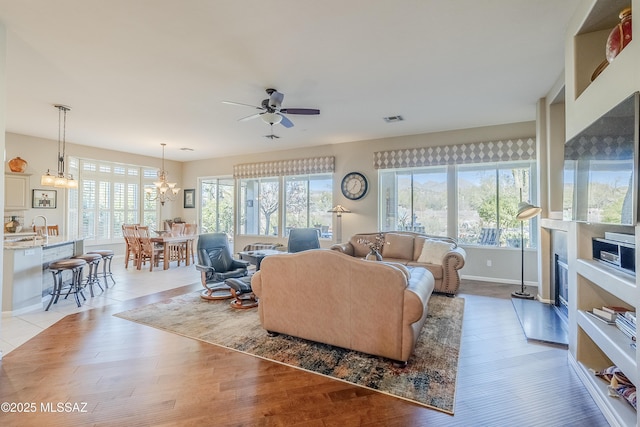 living room with light wood-type flooring, ceiling fan with notable chandelier, and a wealth of natural light