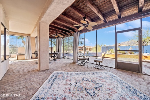 unfurnished sunroom featuring wooden ceiling, ceiling fan, and beamed ceiling