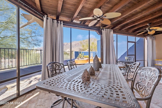 sunroom / solarium featuring wood ceiling, ceiling fan, beamed ceiling, and a mountain view