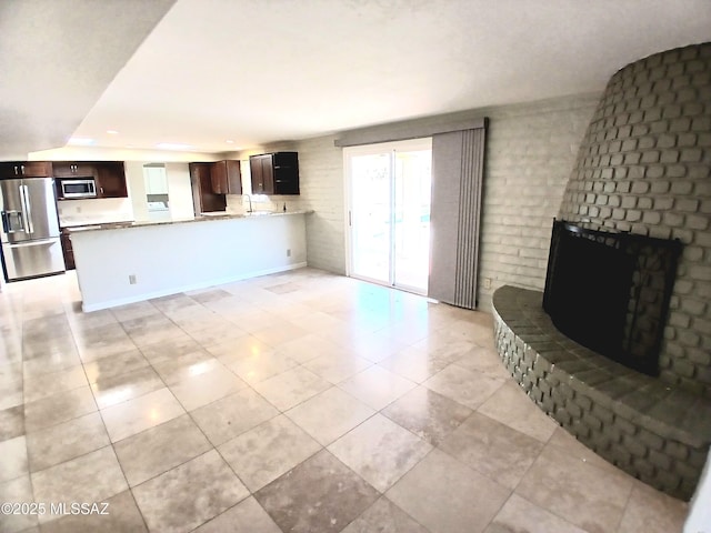 living room featuring brick wall, a fireplace, light tile patterned flooring, and baseboards