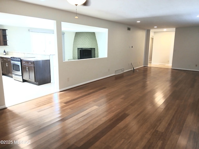 unfurnished living room with dark wood-style flooring, a brick fireplace, visible vents, and baseboards