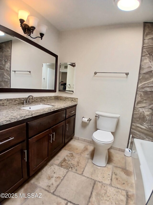 bathroom with toilet, baseboards, stone tile flooring, and vanity